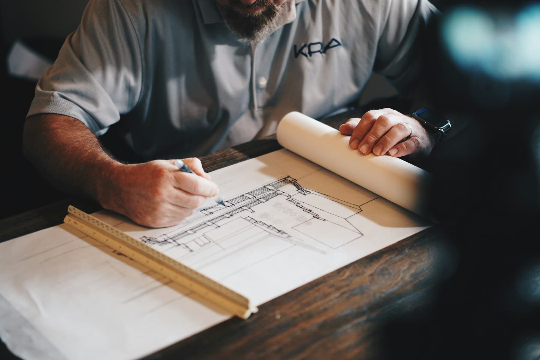 An architectural drawing being developed by hand on a wooden desk